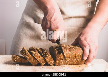 Un uomo affetta un grosso coltello con pane fresco con crosta dorata. Il concetto di cottura a casa cibo dieta senza lievito. Foto Stock