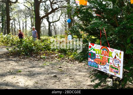 8 aprile 2020, Southborough Common, Kent, UK: Messaggi per bambini che ringraziano il personale NHS e i principali lavoratori appesi su un albero messo in su per lo scopo su Southborough Common durante il governo ha imposto quarantena / blocco per ridurre la diffusione del coronavirus. I bambini di tutto il paese hanno messo messaggi e disegni di arcobaleni nelle finestre e altrove per diffondere la speranza e incoraggiare la gente a rimanere allegra durante la pandemia. Una coppia anziana può essere vista camminare sullo sfondo. Foto Stock