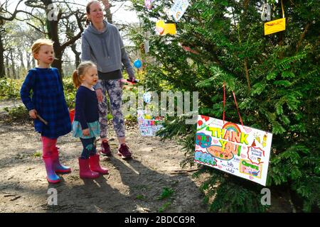 8 aprile 2020, Southborough Common, Kent, UK: Una madre e le sue figlie guardano i messaggi dei bambini ringraziando il personale di NHS e gli operai chiave appesi su un albero messo in su per lo scopo su Southborough Common durante il governo ha imposto la quarantena / blocco per ridurre la diffusione del coronavirus. I bambini di tutto il paese hanno messo messaggi e disegni di arcobaleni nelle finestre e altrove per diffondere la speranza e incoraggiare la gente a rimanere allegra durante la pandemia. Foto Stock