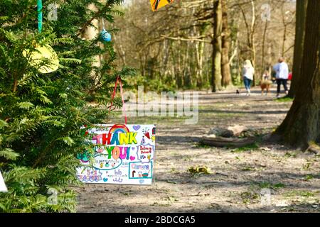 8 aprile 2020, Southborough Common, Kent, UK: Messaggi per bambini che ringraziano il personale NHS e i principali lavoratori appesi su un albero messo in su per lo scopo su Southborough Common durante il governo ha imposto quarantena / blocco per ridurre la diffusione del coronavirus. I bambini di tutto il paese hanno messo messaggi e disegni di arcobaleni nelle finestre e altrove per diffondere la speranza e incoraggiare la gente a rimanere allegra durante la pandemia. Due donne che camminano i loro cani possono essere visti sullo sfondo. Foto Stock