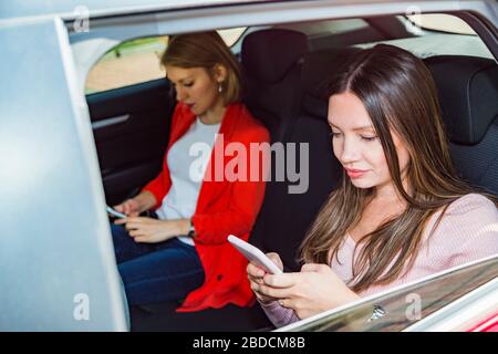 Due ragazze girano insieme in auto usando i loro telefoni Foto Stock