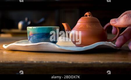 Bella cerimonia del tè cinese con pentola di argilla rossa e piccola tazza su piatto di ceramica bianca fatta a mano con mano maschile Foto Stock