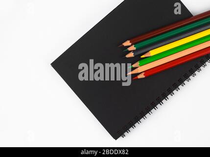 Alcuni pastelli a matita di colore diverso sparsi sopra un diario isolato di carta nera Foto Stock