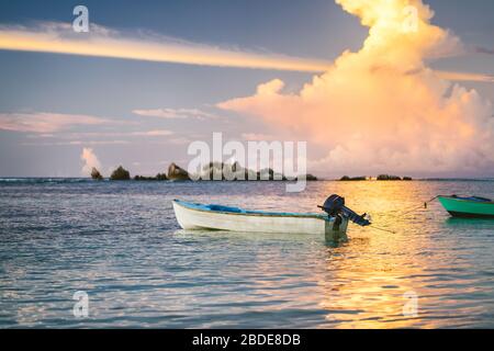 Nuvole dorate viola illuminate dal tramonto su la Digue. Una barca da pesca galleggia nella baia dell'oceano con i colori del fuoco all'orizzonte Foto Stock