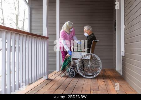 Donna e uomo in sedia a rotelle indossano una maschera protettiva per prevenire trasmissione del coronavirus sul portico Foto Stock