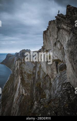 Norvegia, Senja, Man in piedi sul bordo di ripida scogliera sulla cima della montagna Segla Foto Stock