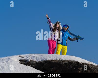 Coppia su una cima di montagna durante una pausa in una stazione sciistica. Sport, concetto di stile di vita sano e attivo. Donna che mostra qualcosa con un dito. Foto Stock