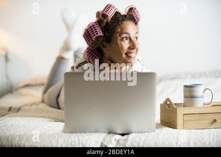 Donna con arricciacapelli sdraiata sul letto con computer portatile Foto Stock