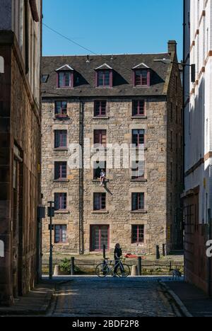 Leith, Edimburgo, Scozia, Regno Unito. 8 Aprile 2020. Covid-19 Lockdown: In uno dei giorni più caldi di sole finora quest'anno con persone in Lockdown. Un uomo e il suo cane siedono precariosamente in una finestra aperta del terzo piano nel magazzino cooperage convertito in appartamenti sulla Shore lungo l'acqua di Leith Foto Stock