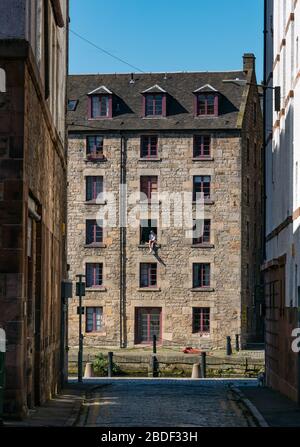 Leith, Edimburgo, Scozia, Regno Unito. 8 Aprile 2020. Covid-19 Lockdown: In uno dei giorni più caldi di sole finora quest'anno con persone in Lockdown. Un uomo e il suo cane siedono precariosamente in una finestra aperta del terzo piano nel magazzino cooperage convertito in appartamenti sulla Shore lungo l'acqua di Leith Foto Stock