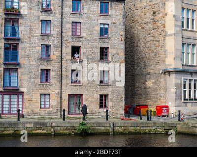 Leith, Edimburgo, Scozia, Regno Unito. 8 Aprile 2020. Covid-19 Lockdown: In uno dei giorni più caldi di sole finora quest'anno con persone in Lockdown. Un uomo e il suo cane siedono precariosamente in una finestra aperta del terzo piano nel magazzino cooperage convertito in appartamenti sulla Shore lungo l'acqua di Leith Foto Stock