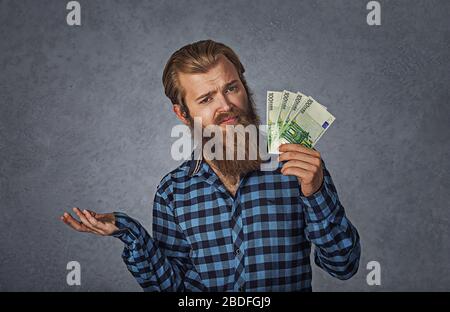 I soldi non portano la felicità del buy. Closeup ritratto giovane uomo in possesso di euro denaro contante shrugging spalle che si preoccupa così ciò che non so gesture isola Foto Stock