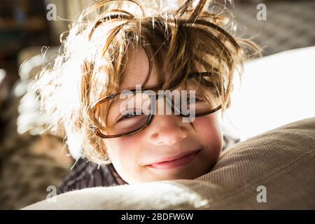 Ritratto di un ragazzo di sei anni con capelli disheveled e occhiali oversize che si svegliano. Capelli del copriletto. Foto Stock