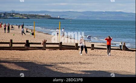 Portobello Beach, Edimburgo, Scozia, Regno Unito. 8 aprile 2020. 18 gradi e il sole pieno hanno portato i Sunworshippers al mare, la maggior parte delle distanze sociali, ma non la folla che ci si aspetterebbe se non ci fosse il Coronavirus Lockdown sul posto e la gente era principalmente a piedi o seduto piuttosto che sdraiarsi sulla sabbia prendere il sole. Un ufficiale di polizia maschile e femminile sul lungomare per un passaggio di routine. Credit: Arch White/Alamy Live News Foto Stock