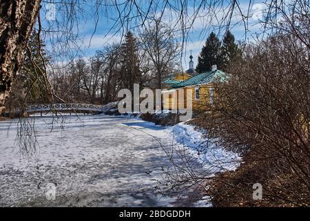 Un ponte con ringhiera in legno nella tenuta della famiglia Pushkin. Lo stagno è coperto di ghiaccio e neve. Il ponte ha una forma arcuata. Russia Foto Stock