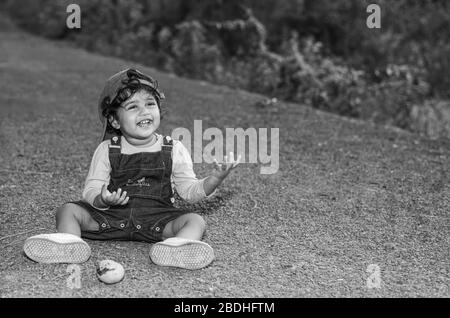 Margao, Goa/India - 2 Aprile 2020 : giocosa ragazza indiana Pretty bambino/neonato indossando un cappuccio, leggendo un libro e giocando avendo campi e tramonto nel backg Foto Stock