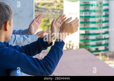 La famiglia applaude il personale medico dal loro balcone. Persone che si aggrachiano su balconi e finestre a sostegno degli operatori sanitari Foto Stock