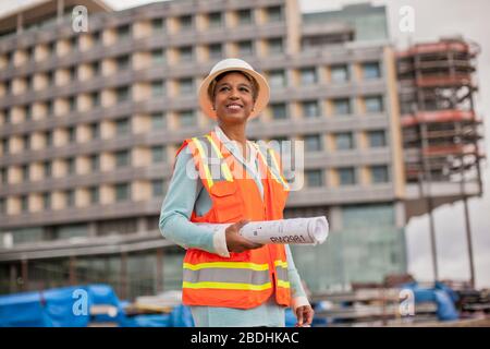 Orgoglioso giovane ingegnere femmina tenendo un rotolo di piani di costruzione su un sito in costruzione. Foto Stock