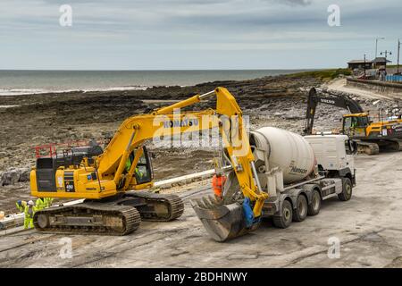 PORTHCATWL, GALLES - GIUGNO 2018: Betoniera che scarica calcestruzzo preconfezionato nella benna di un escavatore per impieghi pesanti per le difese marine Foto Stock