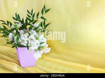 Delicato bouquet di freesia bianca in un cesto di lilla su fondo giallo. Auguri di primavera. Spazio di copia Foto Stock