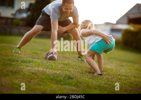 Uomo adulto medio che gioca il calcio americano con sua figlia su un prato. Foto Stock