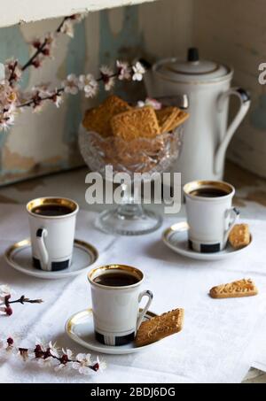 Caffè servito con biscotti shortbread e dolci sullo sfondo di rami fioriti e un vecchio armadio. Foto Stock