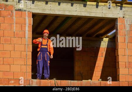 Abbastanza per oggi. Routine quotidiana alla costruzione. Bravo. Riparatore stanco costruttore rilassante in cantiere. Pausa e relax. Uomo barbuto in uniforme ingegnere e elmetto. Giorno normale. Foto Stock