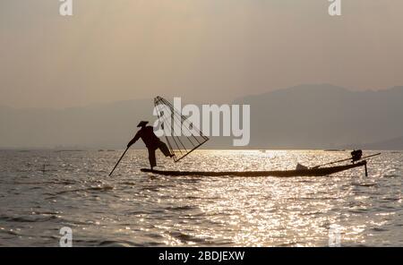 Silhouette di un pescatore Intha con cesto sul lago Inle, Myanmar Foto Stock