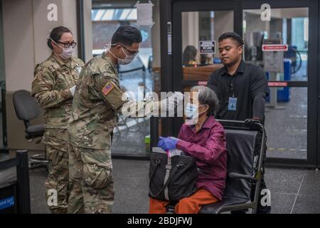 Soldati della Guardia Nazionale dell'Esercito delle Hawaii, passeggeri in partenza all'Aeroporto Internazionale Daniel K. Inouye il 7 aprile 2020 a Honolulu, Hawaii. I soldati assistono il personale dei pompieri dell'aeroporto con lo screening del 100% dei viaggiatori in arrivo e in partenza, per includere i viaggi tra le isole. Foto Stock