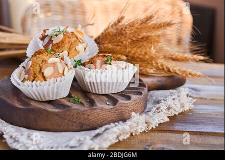 Deliziosi muffin fatti in casa alla cannella di cocco e foglie di caraway su vecchio vassoio bianco concetto di cibo sano con spazio per le copie. Sullo sfondo di spighe secche di grano. Nello stile di rustico Foto Stock