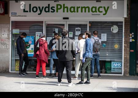 Le persone si accodano al di fuori di una Lloyds Pharmacy a Tottenham, North London, durante il blocco COVID-19, Londra, Inghilterra, Regno Unito Foto Stock