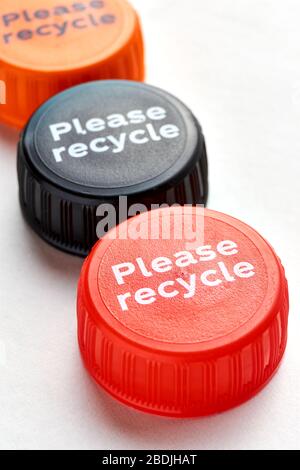 Tappi per flaconi neri, arancioni e rossi con messaggio di riciclo su sfondo bianco. Concetto di inquinamento plastico. Foto Stock