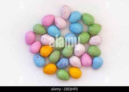 Caramelle al cioccolato con vista dall'alto. Dolci multicolore sotto forma di uova di Pasqua su sfondo bianco. Caramelle blu, gialle e verdi. Foto Stock