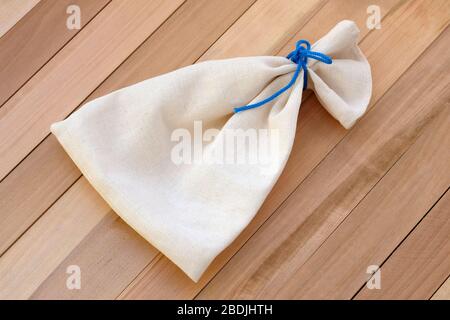 Borsa in lino beige con pizzo blu su fondo in legno. Una piccola borsa in tessuto con lacci. Borse regalo per riporre giocattoli, piccoli oggetti, erbe secche. Foto Stock