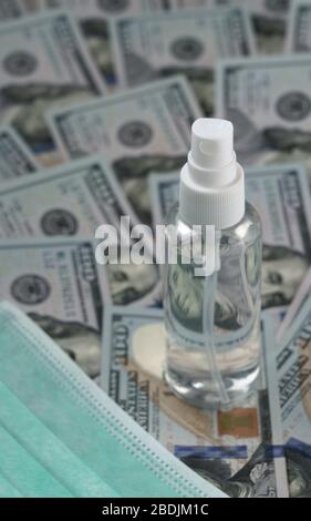 Bottiglia spray di alcol su cento banconote dollari e maschera facciale Foto Stock