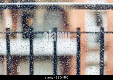 Raindrops su una finestra su uno sfondo di recinzione sfocata durante la quarantena domestica Foto Stock