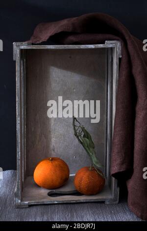 Due tangerini secchi in una scatola decorativa in legno capovolta su fondo nero. Spazio di copia Foto Stock