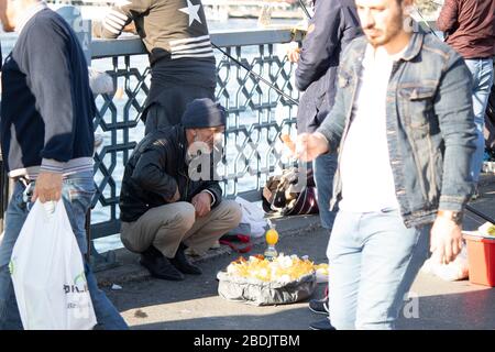 Un vecchio fornitore che vende macchine per spremere il succo di limone. La gente passa intorno all'uomo che ha una sigaretta in bocca. Foto Stock