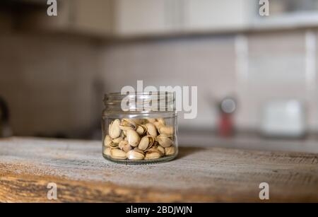Pistacchi in un vaso che si trova su un tavolo bianco vintage con una cucina sullo sfondo. Il pistacchio è un alimento nutriente sano della proteina vegetariana Foto Stock