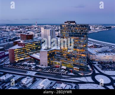 Dall'alto di edifici alti illuminati contemporanei e strade innevate nel quartiere moderno della città di Reykjavik situato vicino al mare in serata d'inverno Foto Stock