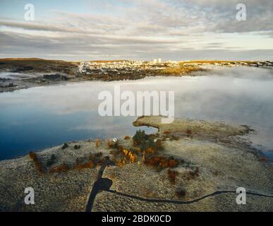 Dall'alto vista del drone della costa nebbiosa del mare con moderna città costiera sullo sfondo in un giorno nuvoloso di autunno in Islanda Foto Stock
