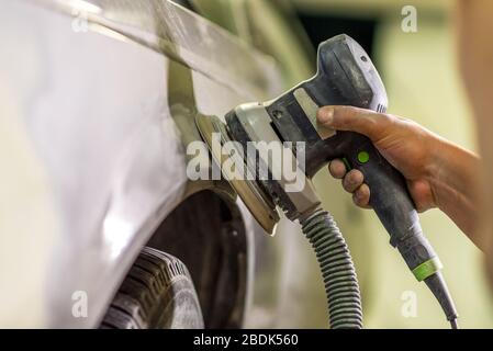 Grinder nelle mani di un uomo che affilare una vernice per auto in auto shop. Foto Stock