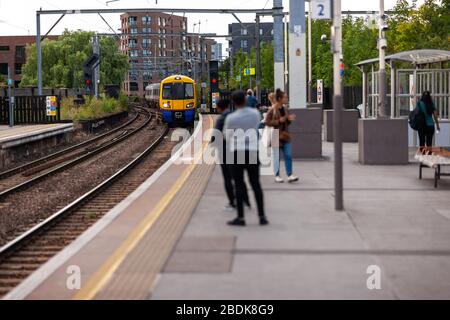 I treni sotterranei e terrestri sono parte integrante del sistema di transito Englands, come questi passeggeri che attendono alla stazione di Camden Road a Londra. Foto Stock