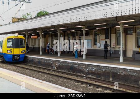 I treni sotterranei e terrestri sono parte integrante del sistema di transito Englands, come questi passeggeri che attendono alla stazione di Camden Road a Londra. Foto Stock