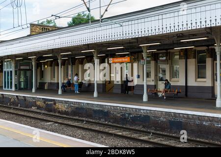 I treni sotterranei e terrestri sono parte integrante del sistema di transito Englands, come questi passeggeri che attendono alla stazione di Camden Road a Londra. Foto Stock