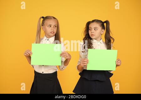 Riflettendo su un lavoro a casa. Figlioli holding fogli vuoti per esame lavoro su sfondo giallo. Le piccole bambine con vuoto libri verdi per il lavoro di progetto o di ricerca. La carta funziona, copiare lo spazio. Foto Stock