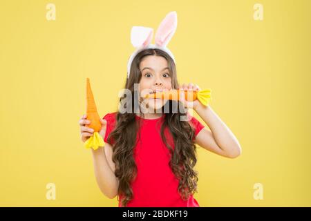 Tradizione primaverile. Bambino sfondo giallo. Le vacanze di Pasqua stanno arrivando. Cibo sano. Orecchie di coniglio per bambini. Dieta per la salute. Beneficio di mangiare carota. Carota di Pasqua. Ragazza tenere carota. Gioca con il cibo. Foto Stock