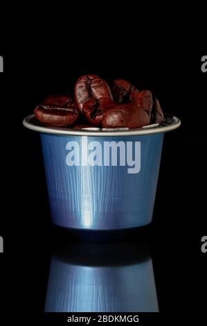 capsula di caffè di colore blu con chicchi di caffè tostati e il loro riflesso su una superficie su sfondo nero Foto Stock