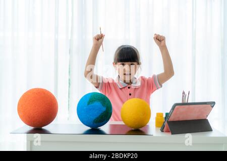 Il braccio della scolaretta elementare asiatica solleva per sucess la pittura del modello del sistema solare imparare circa il sistema solare via video conferenza con l'insegnante a casa Foto Stock