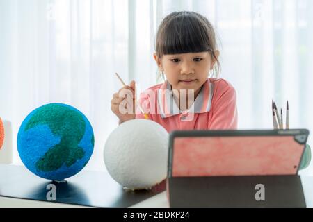 Scuola elementare asiatica dipingere la luna in classe di scienza imparare circa il sistema solare tramite video conferenza con l'insegnante e altri compagni di classe Foto Stock